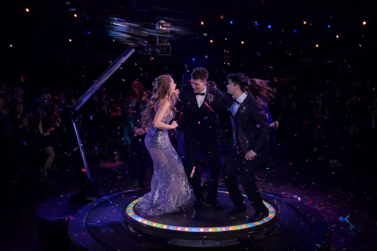 Friends in prom outfits dancing on an illuminated 360 video booth platform as the camera arm spins