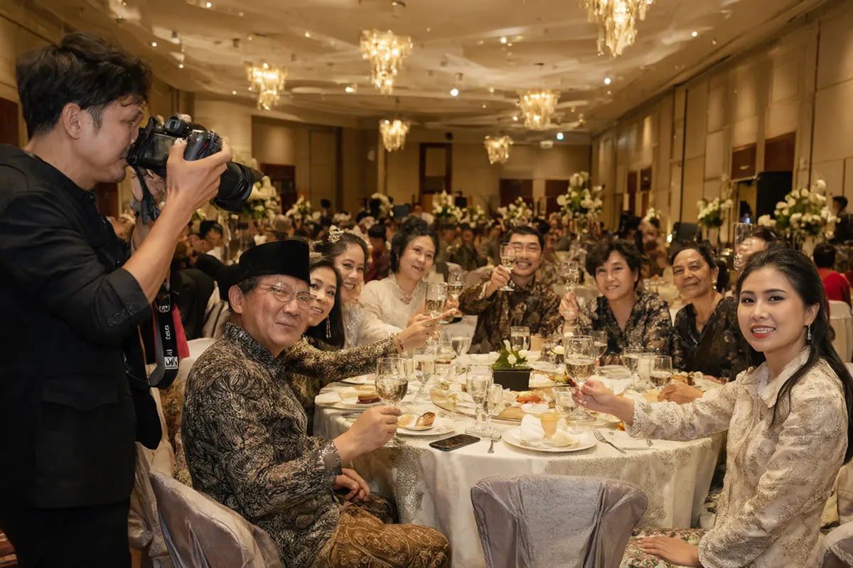 Fotografer keliling memotret tamu yang duduk di meja bundar resepsi pernikahan
