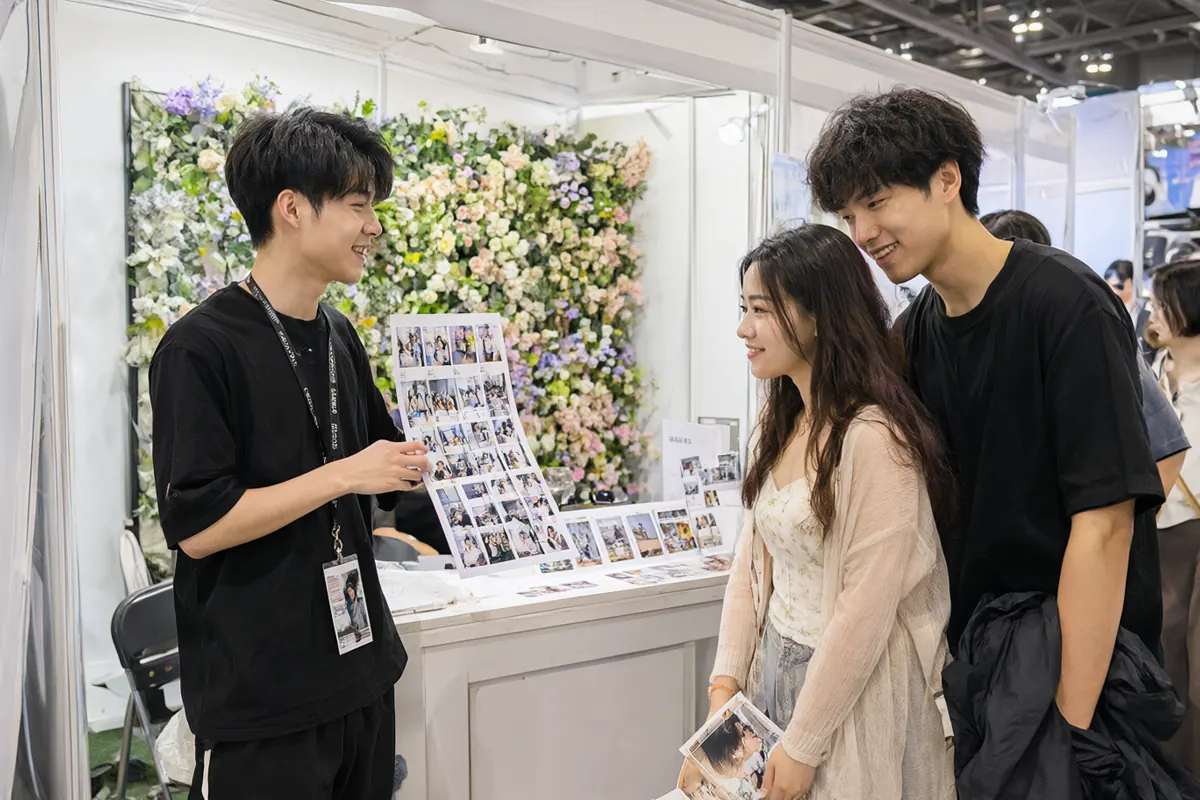婚博会上拍照亭商家向一对新人展示照片条样品